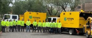 Titan tree care crew standing in front of bright yellow company trucks in a parking area, wearing high-visibility safety gear.