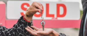 House keys are handed over in front of a sign that reads “sold”.