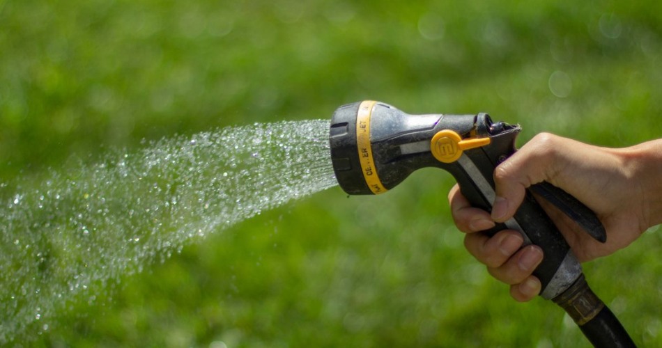 Close-up of garden hose nozzle spraying water over green lawn during summer watering routine.