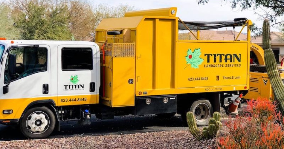 Titan tree care yellow service truck parked in north phoenix residential driveway with desert landscaping and cacti visible in foreground.