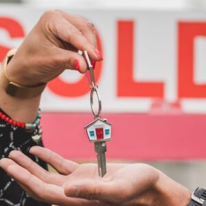 House keys are handed over in front of a sign that reads “SOLD”.